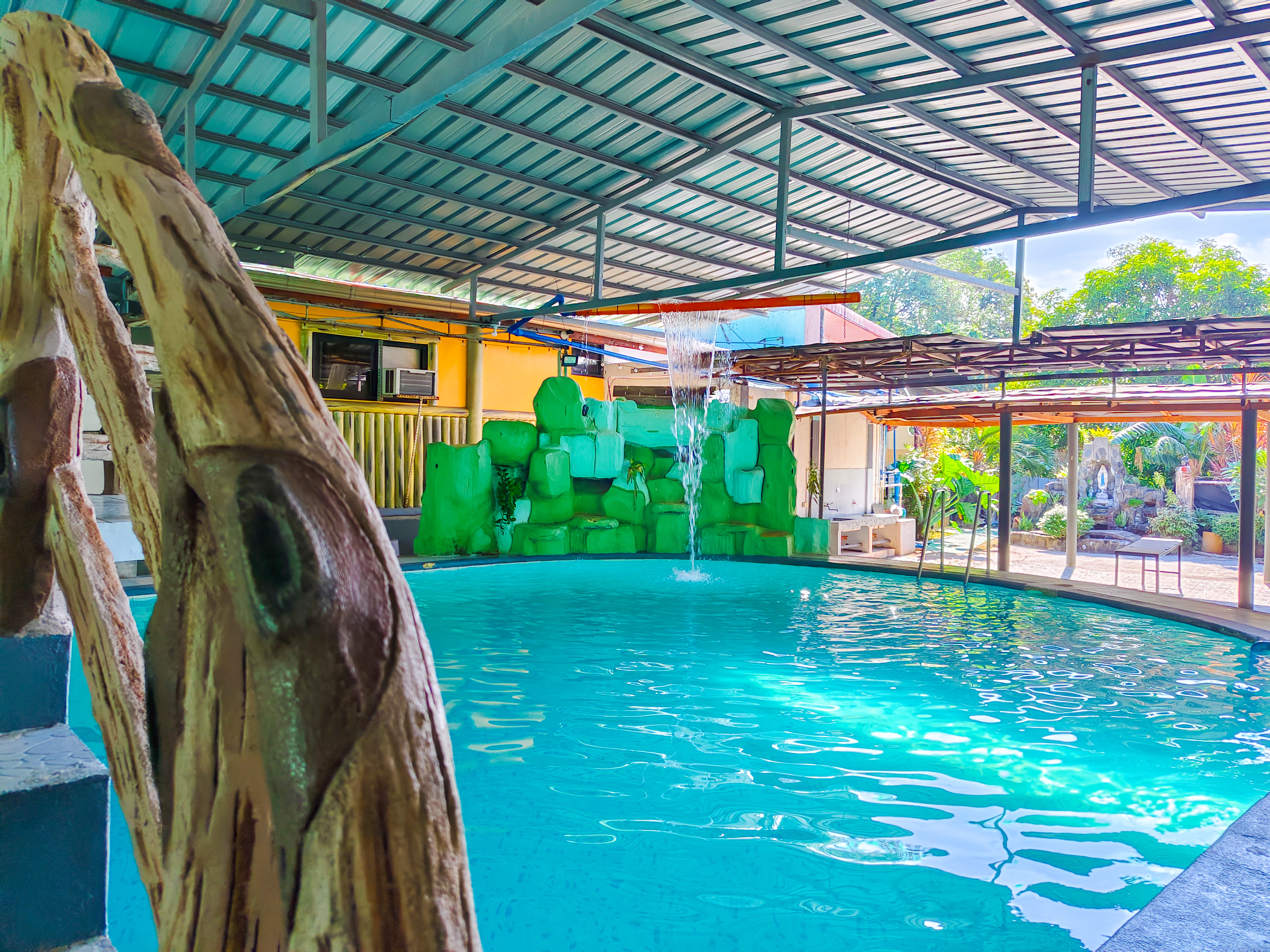 Beautiful indoor swimming pool at Emerald Resort with a cascading waterfall, wooden railing, and vibrant green rock formations, offering a relaxing atmosphere.